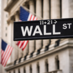 Wall Street street sign in New York with American flags and the New York Stock Exchange building in the background.